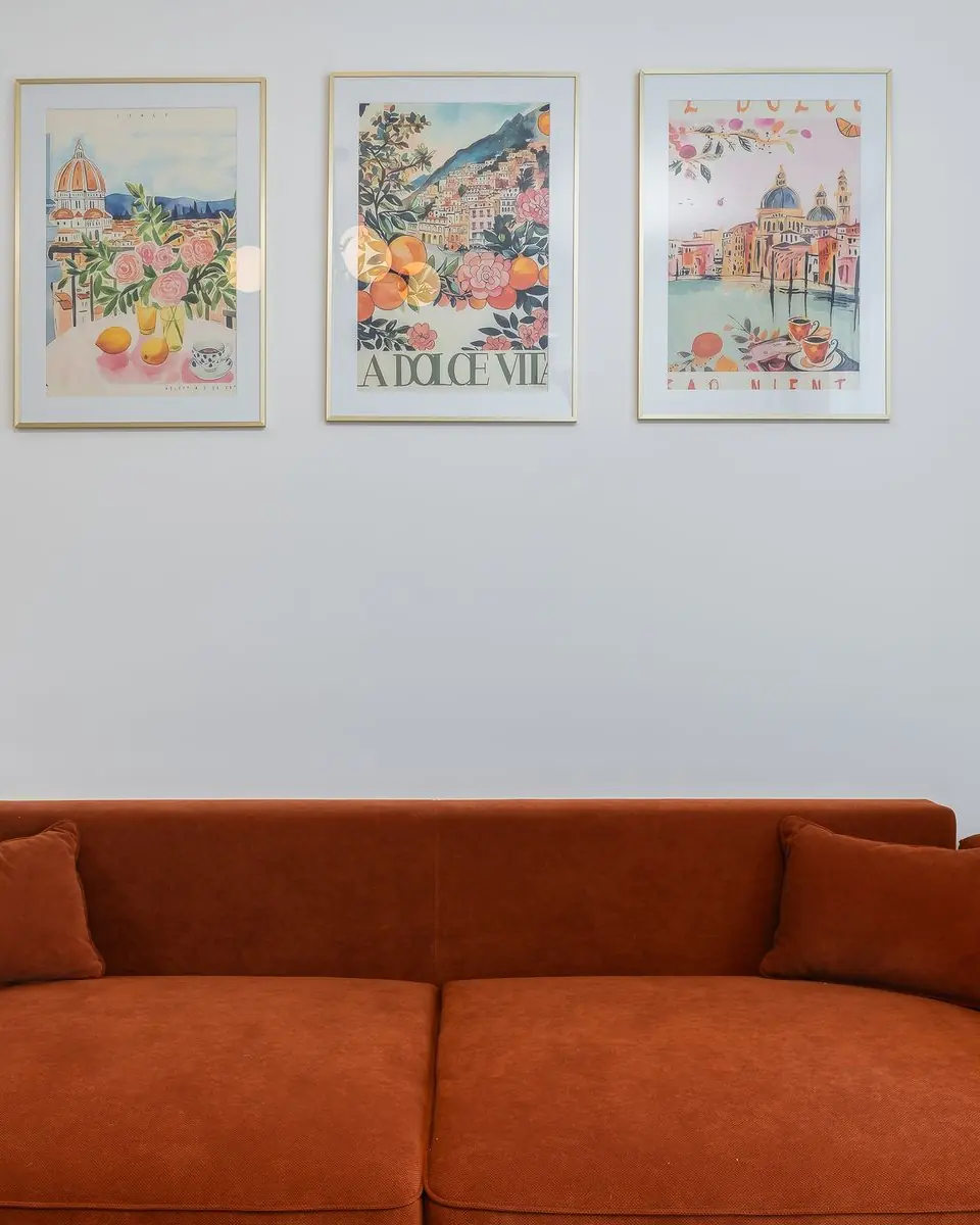 Framed prints on a wall above an orange sofa